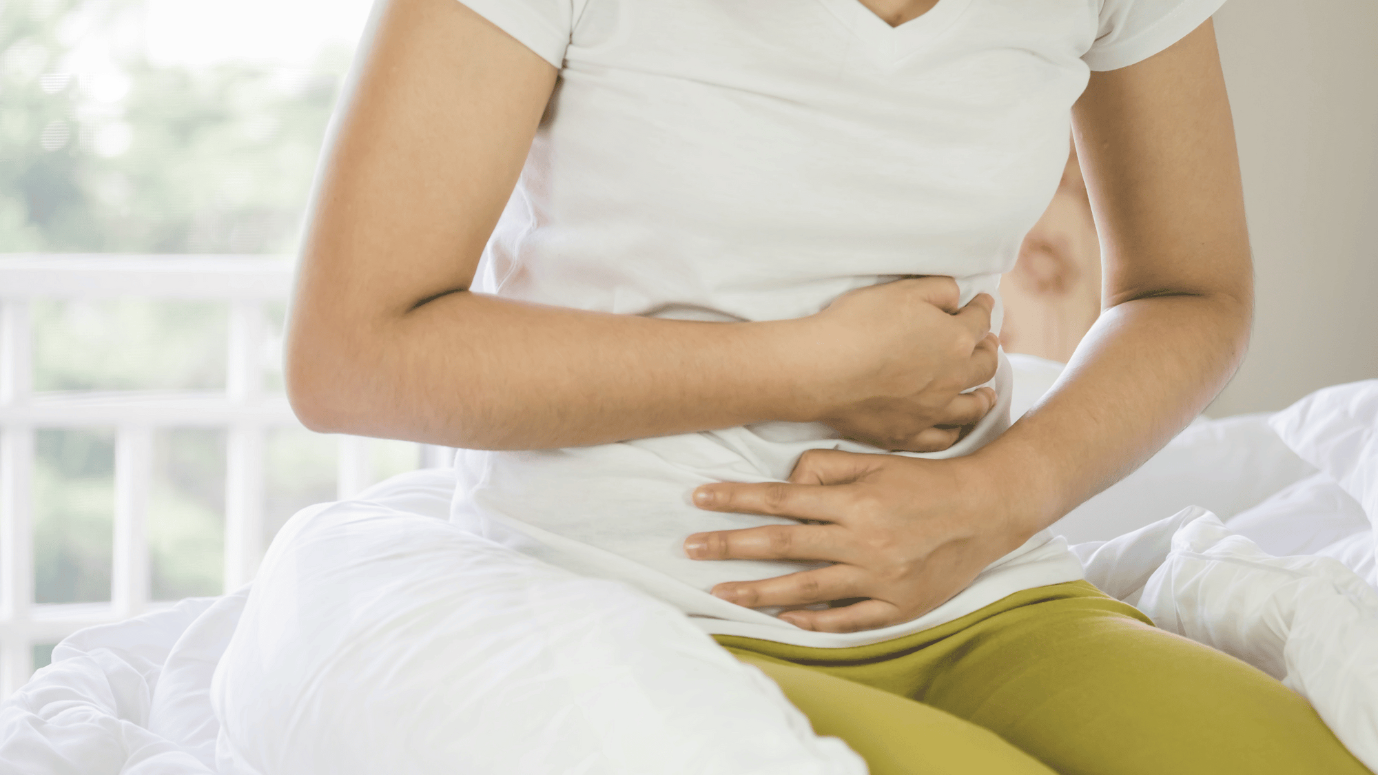 woman in bed gripping her stomach while wearing green pants