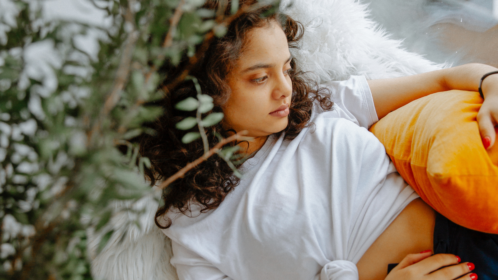 Woman in an orange top sitting quietly and looking down, reflecting the subtle and often overlooked hidden signs of hormonal imbalance in women
