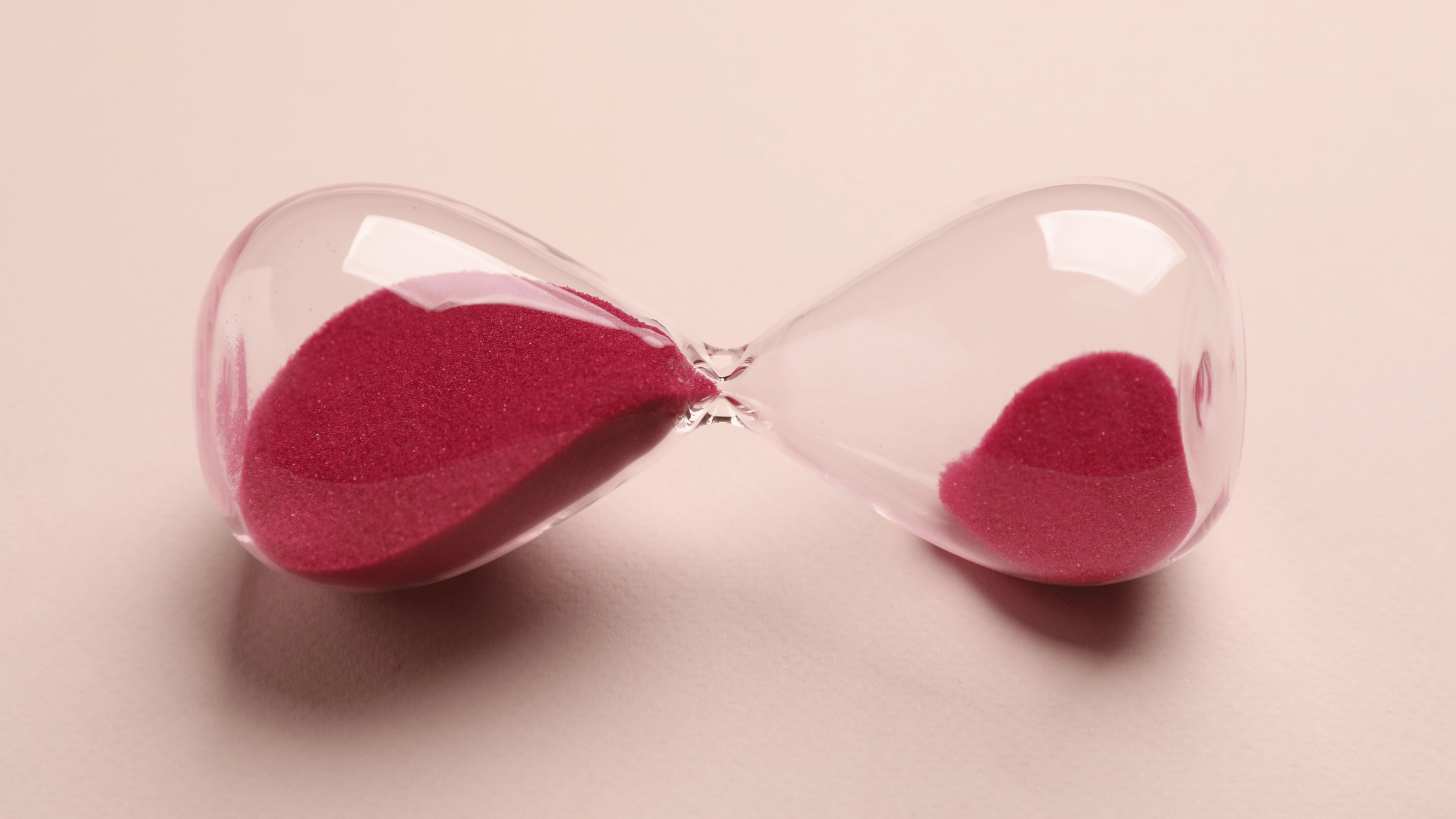 Red hourglass with sand against a soft peach background, symbolizing the role of time and process in supporting healthy estrogen metabolism naturally