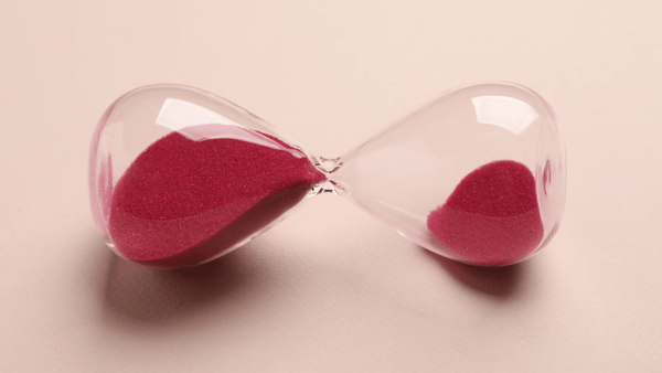 Red hourglass with sand against a soft peach background, symbolizing the role of time and process in supporting healthy estrogen metabolism naturally