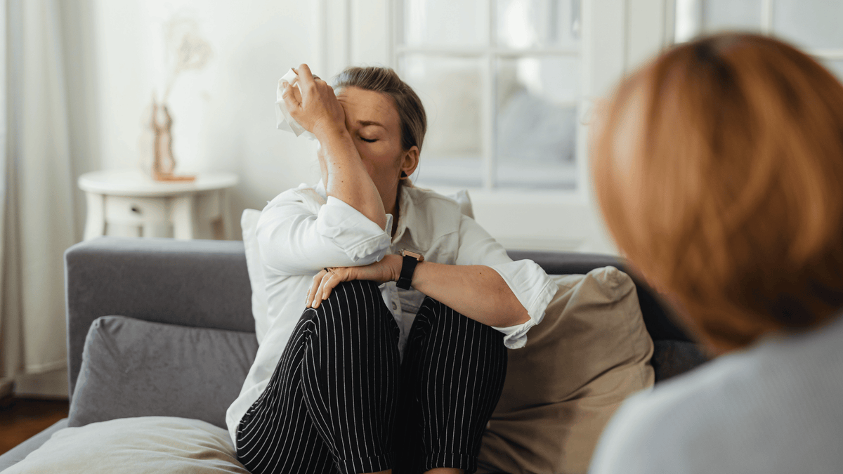 Woman sitting on a couch looking tired and emotionally drained, illustrating common luteal phase symptoms like fatigue, mood swings, and low energy