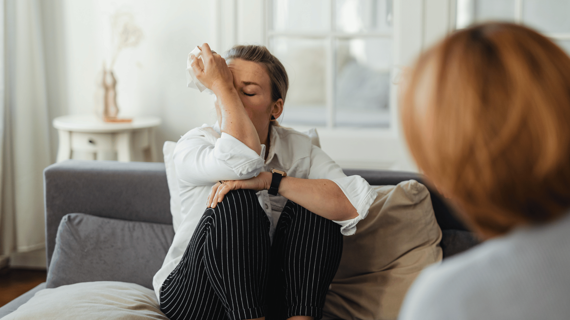 Woman sitting on a couch looking tired and emotionally drained, illustrating common luteal phase symptoms like fatigue, mood swings, and low energy