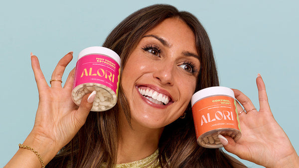 Smiling woman holding two ALORI hormone supplement jars, showcasing the brand's targeted approach to hormone support that goes beyond generic wellness supplements