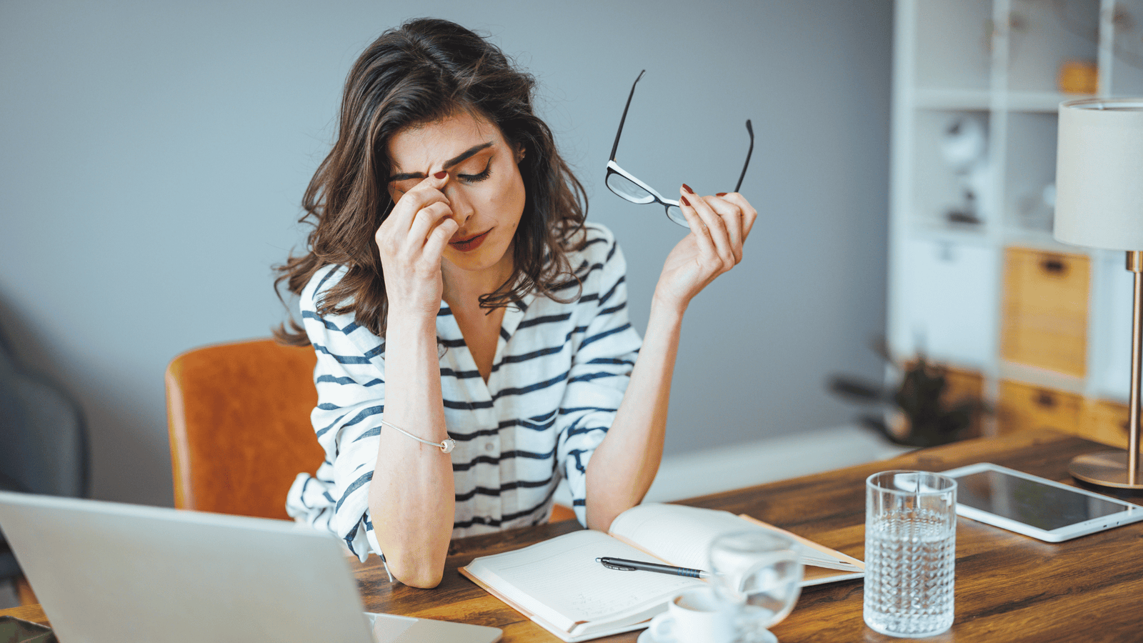 woman sitting at a dStressed woman at her desk rubbing her face and eyes, illustrating the exhaustion, brain fog, and facial puffiness caused by chronically elevated cortisol levelsesk seemingly stressed out working