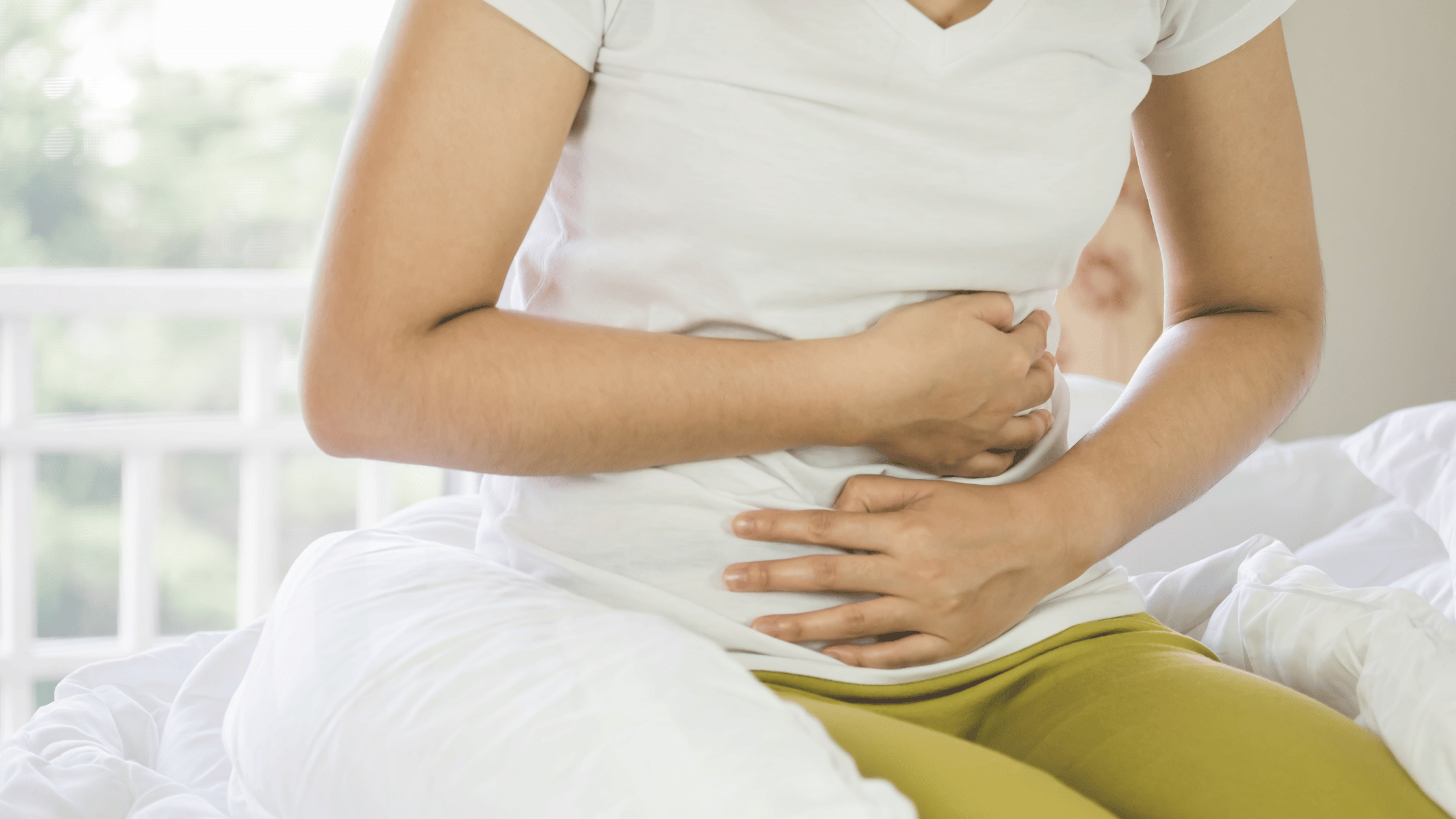 woman in bed gripping her stomach while wearing green pants
