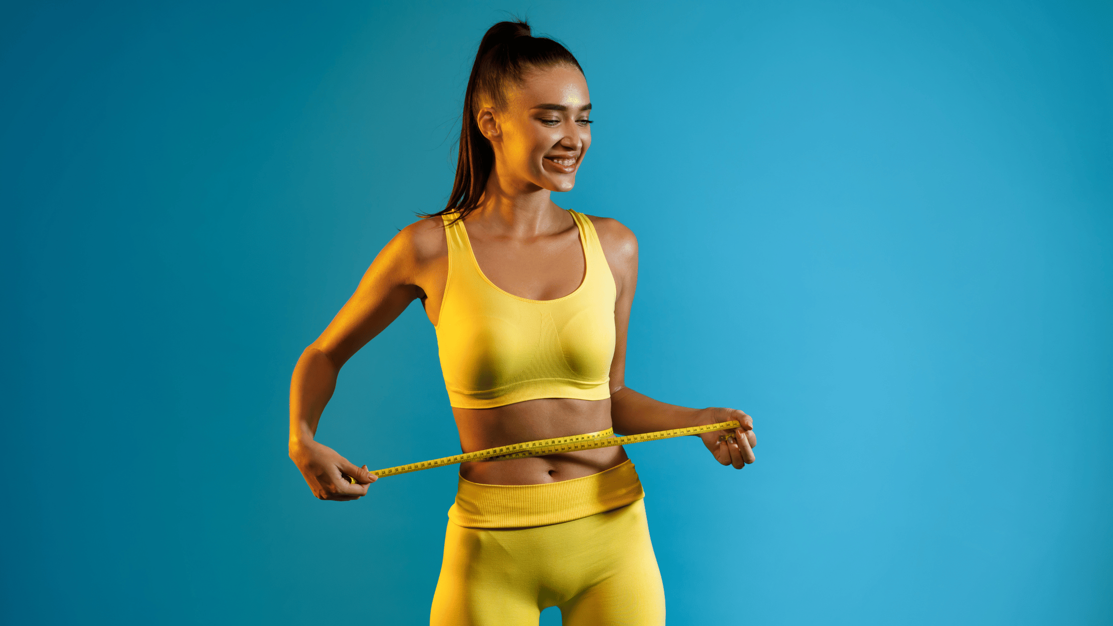 Woman wearing yellow on blue background with measuring tape on stomach